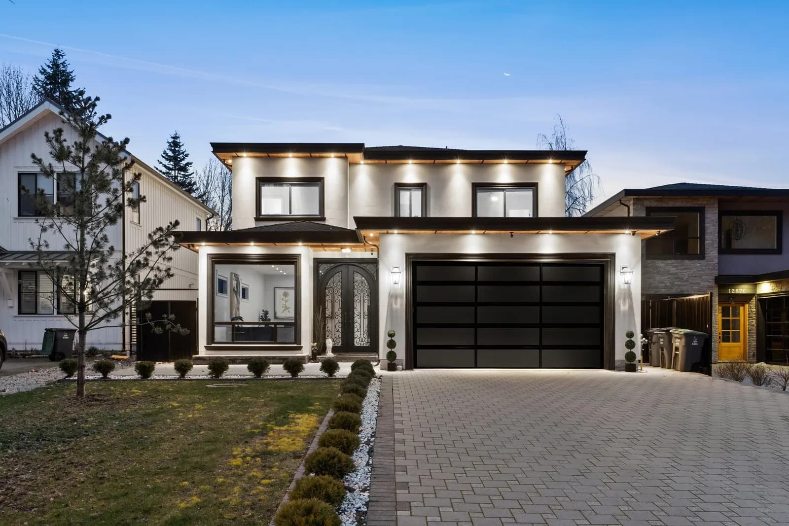 Front exterior at dusk of the custom two-level home at 12686 25 Avenue, Crescent Beach, South Surrey BC — cast iron and glass entry door, paver driveway, built by Pro Construction Group