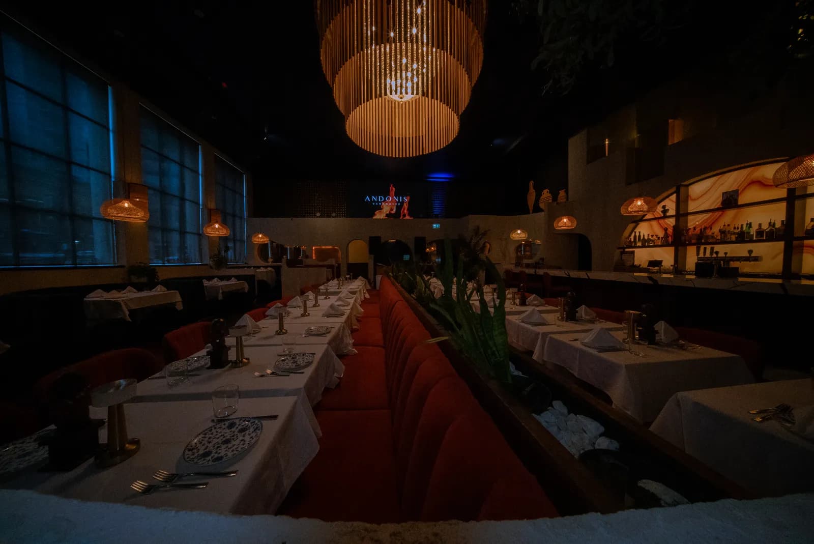 Dining room of Andonis Supper Club at 1193 Granville Street, Vancouver — red banquette seating, rattan pendant chandelier, textured plaster walls and back bar built out by Pro Construction Group