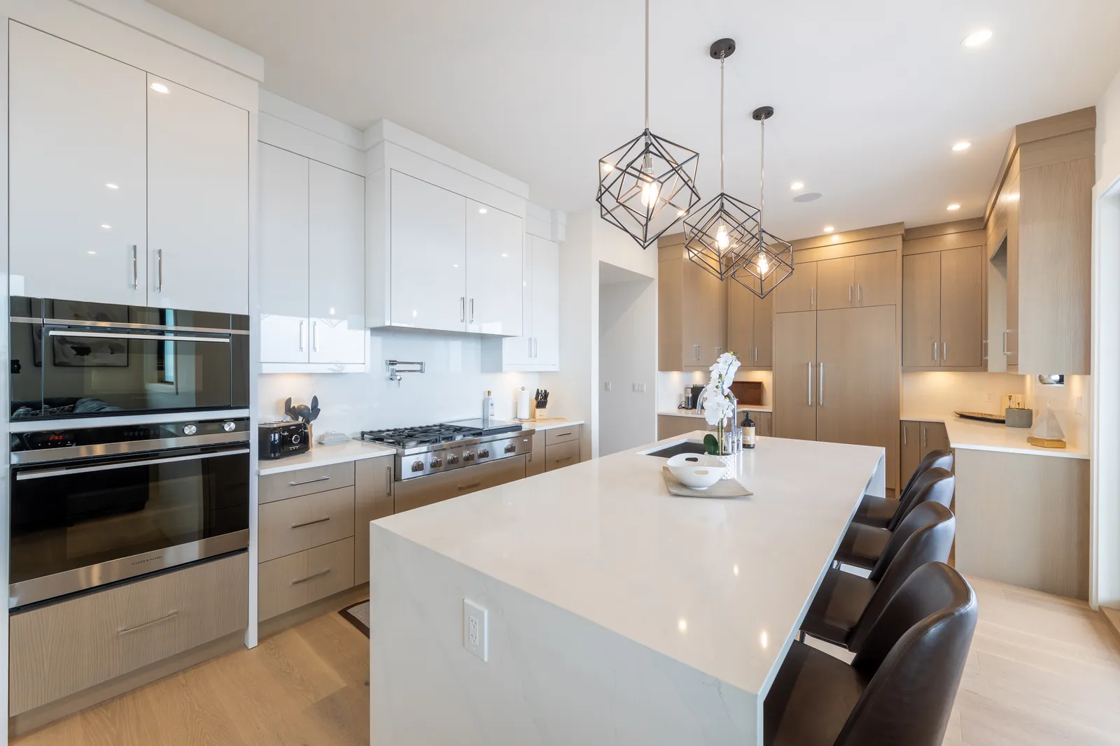 Custom kitchen at 2185 Navigators Rise, Langford BC — waterfall quartz island, two-tone flat-panel cabinetry, built-in wall ovens and geometric pendant lights