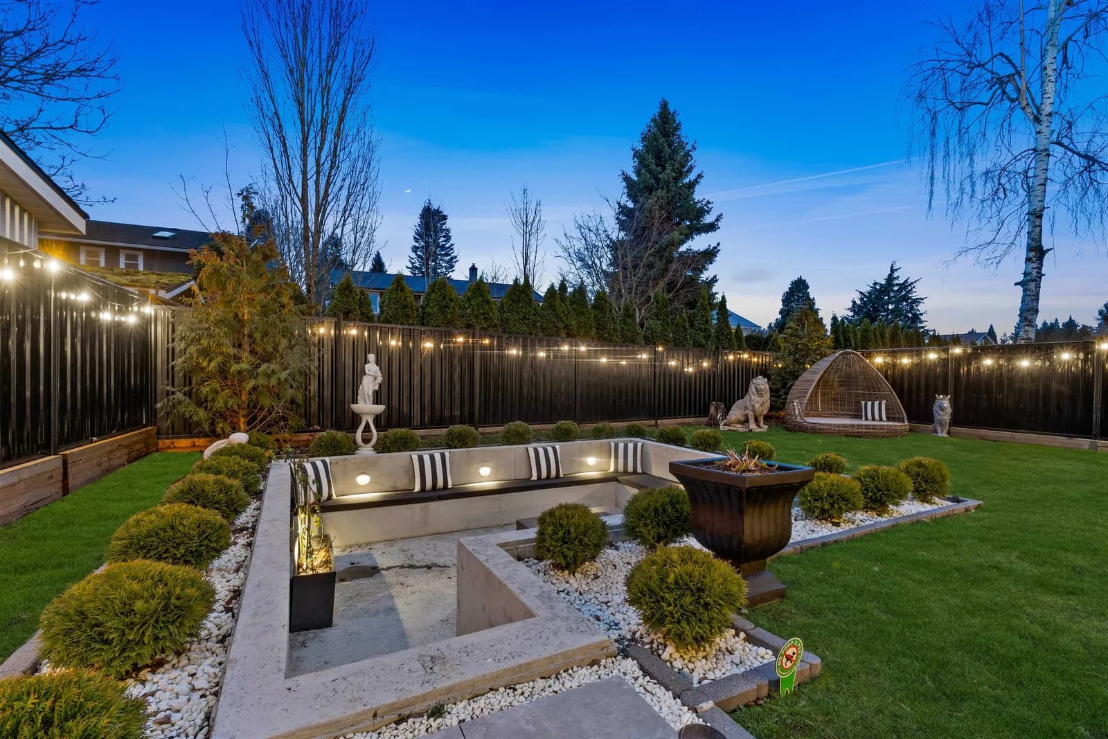 Sunken fire-pit patio with built-in seating, landscaping and string lights behind the Crescent Beach custom home at 12686 25 Avenue, South Surrey